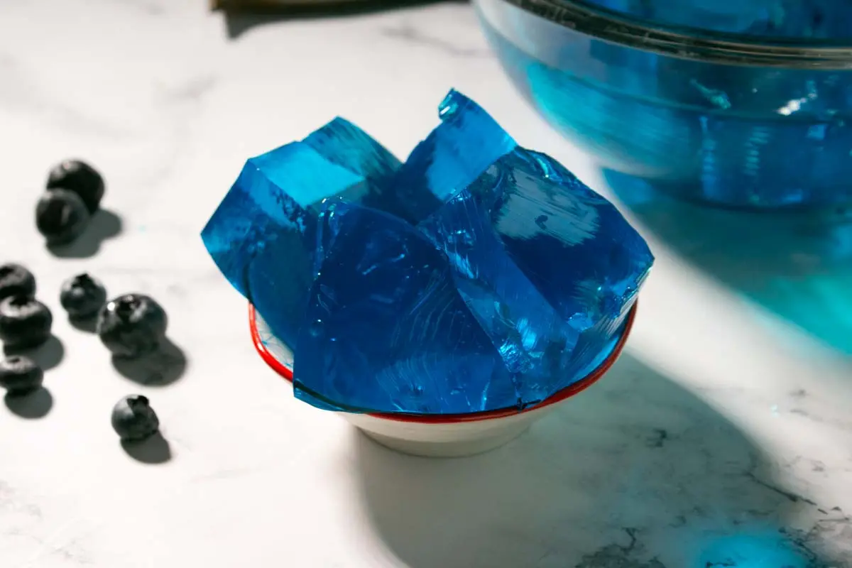 Blue gelatin squares served in a bowl beside blueberries