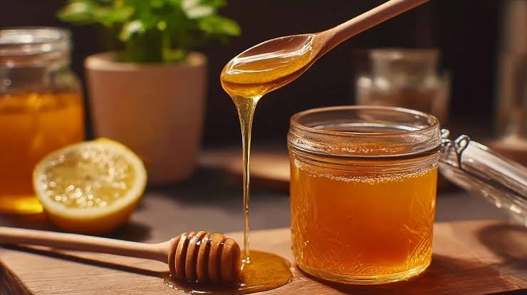 Golden raw honey drizzled into a jar with a fresh lemon slice on a wooden table